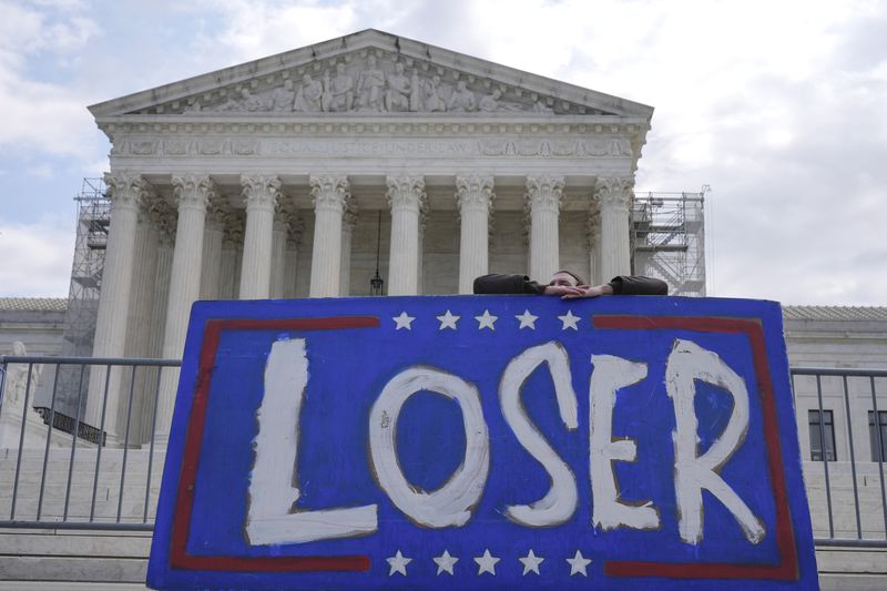A demonstrator stands outside the Supreme Court as the justices prepare to hear arguments over whether Donald Trump is immune from prosecution in a case charging him with plotting to overturn the results of the 2020 presidential election, on Capitol Hill Thursday, April 25, 2024, in Washington. (AP Photo/Mariam Zuhaib)