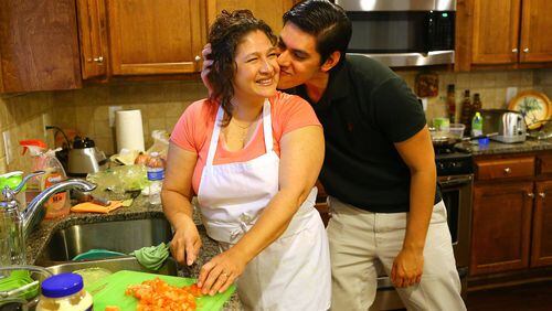 Christian Jimenez gives his mother Maria Velasquez a kiss on the cheek while helping her prepare the family dinner in the kitchen of the family home recently in Buford. CURTIS COMPTON / CCOMPTON@AJC.COM