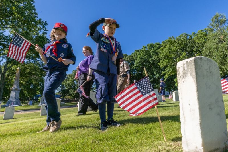 Alec Mayhan, 9,  salutes after placing one of the over 18,000 flags in front of a tombstone at Marietta national cemetery Saturday, May 28, 2022. The flags are planted in front of all the tombstones in preparation for the Memorial Day ceremony Monday. (Steve Schaefer / steve.schaefer@ajc.com