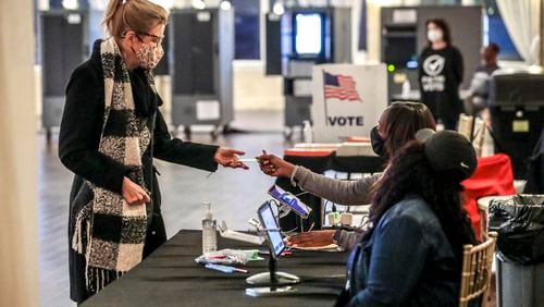 November 30, 2021 Atlanta: Sonya Collins (left) receives her ballot from poll workers, Brandy Allen (center) and Quay Edwards (right) at Park Tavern located at 500 10th St NE in Atlanta on Tuesday, November 30, 2021.  (John Spink / John.Spink@ajc.com)