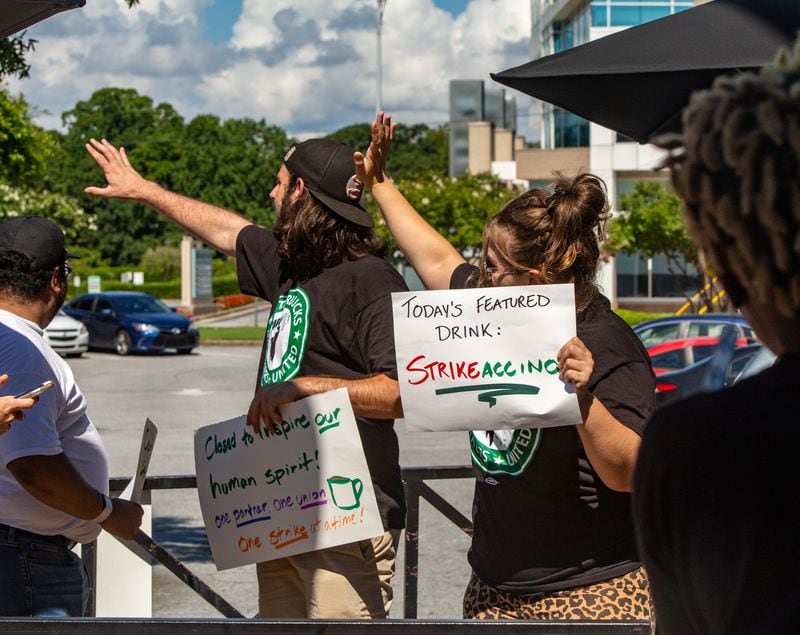 Starbucks employees, union workers and former Starbucks employees, including Nick Julian, far left, Camden Mitchell, center and Aleyah Riggs, right, picket at the Howell Mill location while on strike Sunday, July 17, 2022 after voting to join the union and asking for guaranteed work hours, benefits and a contract to protect the hourly workers.  Starbucks management has not responded to requests to start negotiation.  (Jenni Girtman for The Atlanta Journal-Constitution)