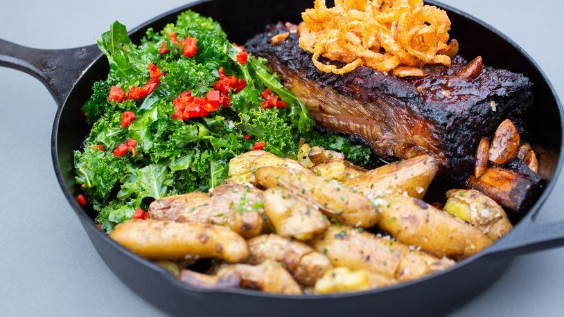 The bone-in short ribs at Adele's is a hefty two-person entree served in a cast-iron skillet with a massive portion of roasted fingerling potatoes and mustard greens. Ryan Fleisher for The Atlanta-Journal Constitution