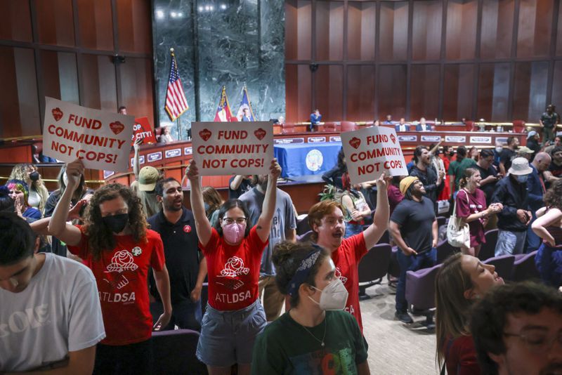 Protestors turn their back and hold “Fund Community Not Cops!,” signs as council member Michael Julian Bond speaks during the public comment portion ahead of the final vote to approve legislation to fund the training center, on Monday, June 5, 2023, in Atlanta. (Jason Getz / Jason.Getz@ajc.com)