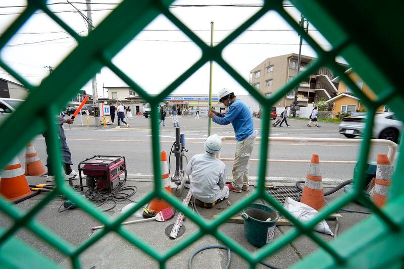 Workers set up a barricade near the Lawson convenience store, background, Tuesday, April 30, 2024, at Fujikawaguchiko town, Yamanashi Prefecture, central Japan. The town of Fujikawaguchiko, known for a number of popular photo spots for Japan's trademark of Mt. Fuji, on Tuesday began to set up a huge black screen on a stretch of sidewalk to block view of the mountain in a neighborhood hit by a latest case of overtourism in Japan. (AP Photo/Eugene Hoshiko)