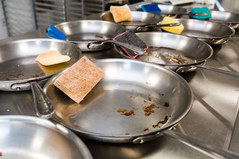 Skillets with hard-to-remove food residue still attached and the sponges used to clean them sit for examination during testing of a range of sponges for an upcoming review.