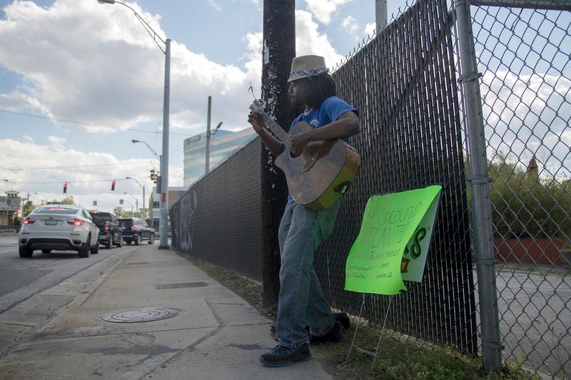 Accompanied by a sign that reads “Be encouraged Atlanta!!! And this too shall pass,” artist Kidesh plays music along Howell Mill Road in Atlanta’s Wildwood neighborhood on Tuesday, April 21, 2020. “I wanted to be a positive influence,” Kidesh said. (ALYSSA POINTER / ALYSSA.POINTER@AJC.COM)