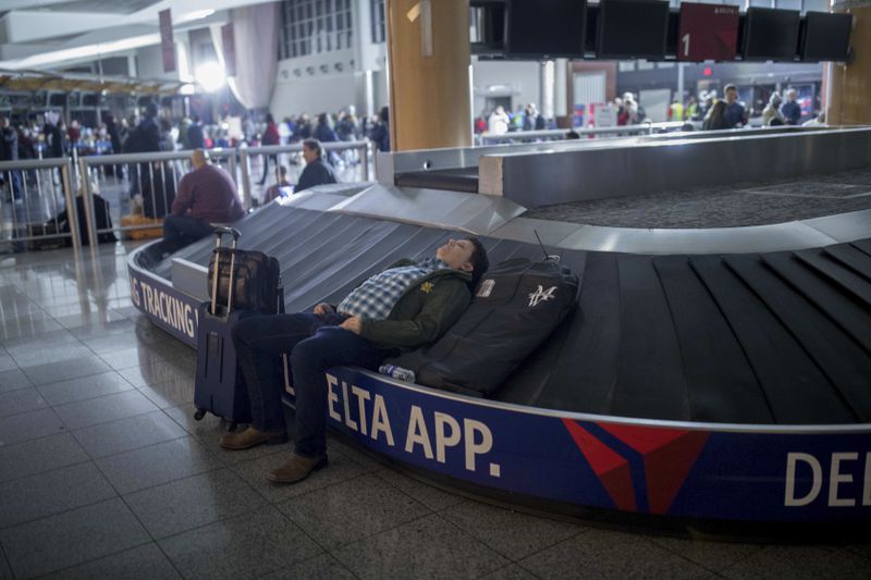 A traveler sleeps on a baggage carousel at Hartfield-Jackson Atlanta International Airport, Sunday, Dec. 17, 2017, in Atlanta. A sudden power outage at the airport on Sunday grounded scores of flights and passengers during one of the busiest travel times of the year. 