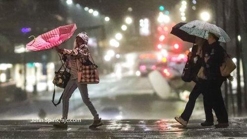 A woman nearly loses her umbrella early Monday morning as she crosses the street at the intersection of Linden Avenue and West Peachtree Street amid rain in downtown Atlanta.