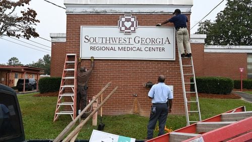 Hospital maintenance staff Jerry Daniels, left, and Jimmie Fair Sr., right, remove the main sign as Bruce Green assists outside the Southwest Georgia Regional Medical Center on Thursday. The hospital has become the 133rd rural hospital to cease operations in the U.S., and the eighth to be shuttered in Georgia, since 2010, according to researchers. (Hyosub Shin / Hyosub.Shin@ajc.com)
