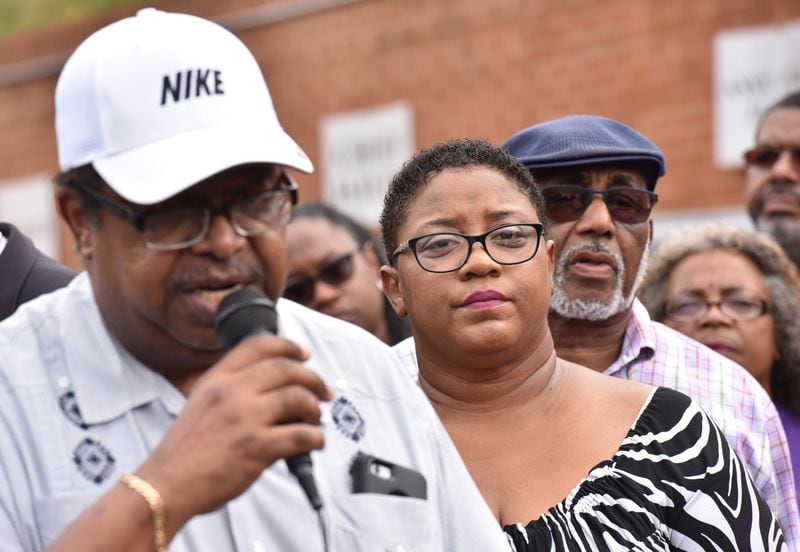 Tamara Cotman (center) listens as the Rev. Timothy McDonald (foreground) speaks to members of the press before she turns herself in outside the Fulton County Jail in Atlanta on Tuesday, October 9, 2018. HYOSUB SHIN / HSHIN@AJC.COM