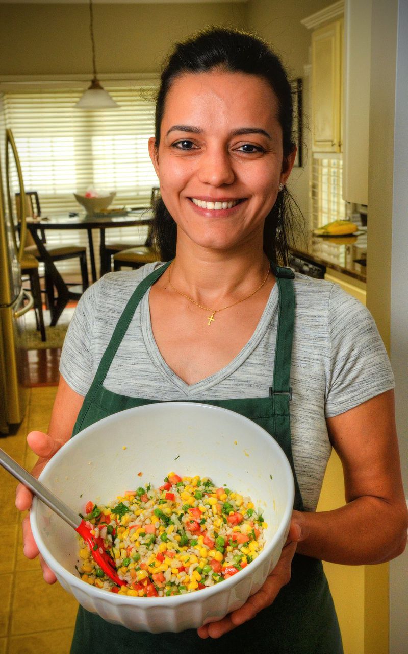 Liliane Chick, who is from Brazil, holds a freshly prepared bowl of her Corn Salad, in which garlic is a key ingredient. STYLING BY LILIANE CHICK / CONTRIBUTED BY CHRIS HUNT PHOTOGRAPHY