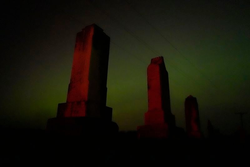 Old tombstones stand against the northern lights at a cemetery early Saturday, May 11, 2024, near Skidmore, Mo. (AP Photo/Charlie Riedel)