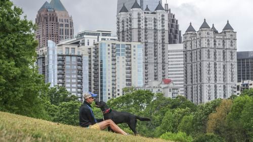 Ron Hoffman sits in Piedmont Park in Midtown with his black labrador retriever, Georgia, on April 14. The above average temperatures Georgia has felt so far this year may continue into summer, a new federal forecast shows. (John Spink / John.Spink@ajc.com)