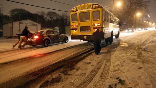 January 28, 2014 Atlanta: People push a car and attempt to push a school bus up an ice-covered University Avenue in Southwest Atlanta on Tuesday evening January 28, 2014 after a winter storm hit the Metro. BEN GRAY / BGRAY@AJC.COM