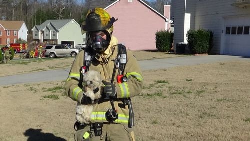 Gwinnett County firefighter Justin Petty carries dog to owner after it was trapped inside a burning home Thursday morning.