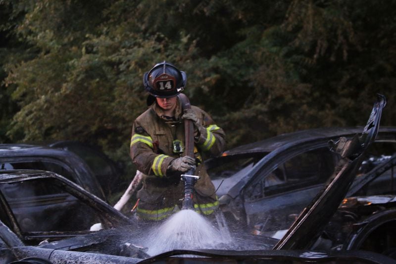 DeKalb County firefighter Joseph Brown works to put out a smoldering car parked at an auto body shop lot near Lithonia. 