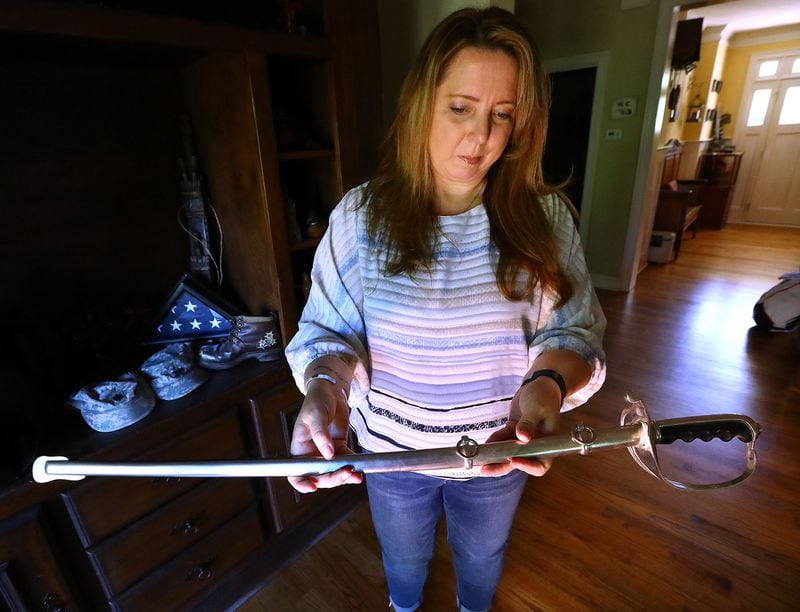 Tammy McCracken holds the sword her husband, David, received when he was promoted to colonel. On the same day he learned of his promotion, doctors performed a biopsy and discovered he had brain cancer. His wife believes his exposure to open-air burn pits in Iraq caused his fatal illness. Curtis Compton/ccompton@ajc.com