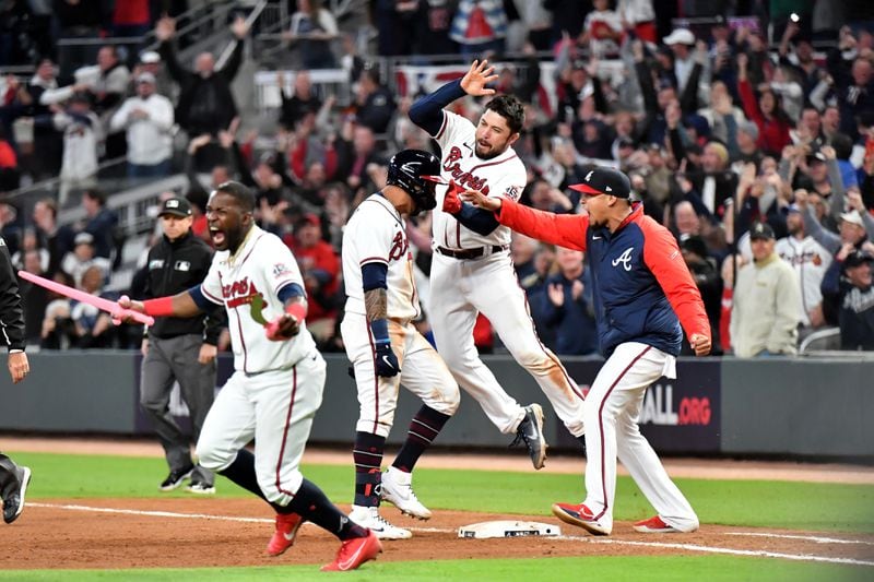 Braves outfielder Guillermo Heredia (left) runs onto field holding a pair of pink swords as teammates celebrate Eddie Rosario after Rosario brought in the game-winning run a single in the ninth inning of Game 2 of the NLCS Sunday, Oct. 17, 2021, at Truist Park in Atlanta. (Hyosub Shin / Hyosub.Shin@ajc.com)