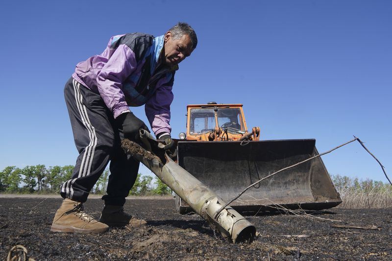 A farmer removes a fragment of a Russian missile as he works on his field in Izium, Kharkiv region, Ukraine, Saturday, April 20, 2024. (AP Photo/Andrii Marienko)