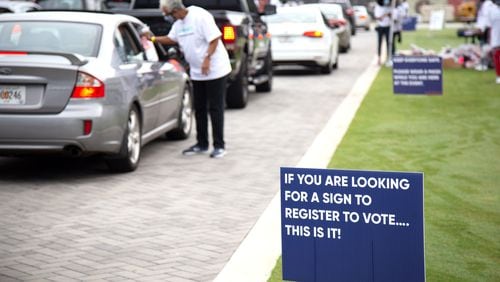 Voter registrations signs line the route at a drive-thru food giveaway at The Home Depot Backyard Saturday, September 26, 2020. Event volunteers helped provide food and groceries to an estimated 2,500 attendees and prepared them to cast their ballots in November. STEVE SCHAEFER / SPECIAL TO THE AJC