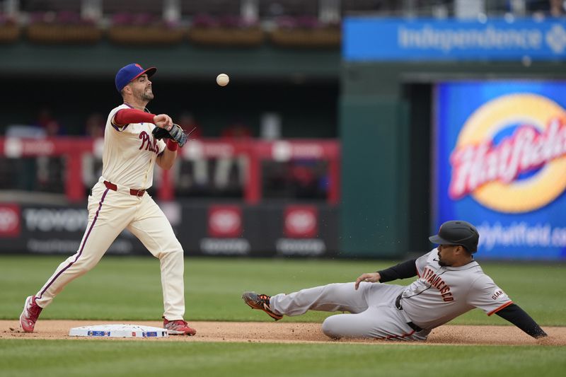 Philadelphia Phillies outfielder Whit Merrifield throws to first base to complete a double play against San Francisco Giants' LaMonte Wade Jr., right, and Wilmer Flores and during the first inning of a baseball game, Monday, May 6, 2024, in Philadelphia. (AP Photo/Matt Rourke)