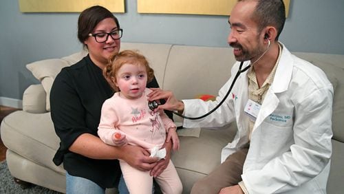 Lisa Maciel, of Hayward, holds her daughter Elyse, 2, as Heal.com pediatrician John Liou examines her on Friday, Jan. 19, 2018 at Maciel’s home in Hayward, Calif. Maciel hired Heal.com to find out if her daughter had a cold or the flu. Many people with the flu are heading to the ER and waiting for hours to see a doctor and running the risk of sitting next to others with even worse cases of the flu. Heal.com gives people another option by sending a primary care doctor to diagnose you at your home or office. (Doug Duran/Bay Area News Group/TNS)
