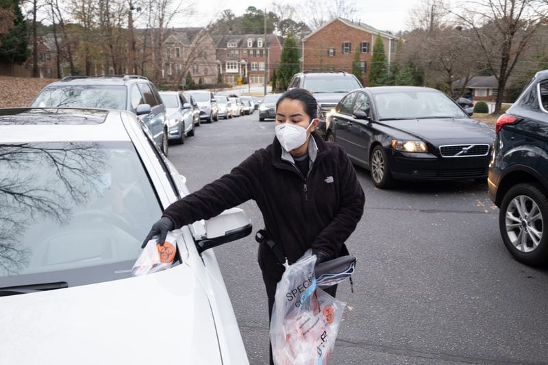 Jamye Velazquez places a testing kit on a customer’s windshield while working at the Viral Solutions drive-through COVID testing site in Decatur on Tuesday. The line stretched more than a block as people prepared for Christmas travel.  (Ben Gray for the Atlanta Journal-Constitution)