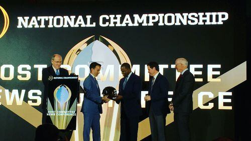 Tampa Bay Sports Commission Executive Director Rob Higgins hands off a ceremonial helmet to Atlanta Mayor Kasim Reed, symbolizing that next season’s College Football Playoff championship game will be played in Atlanta. Also on stage are CFP Executive Director Bill Hancock (at podium), Atlanta Sports Council President Dan Corso (second from right) and Falcons CEO Rich McKay. (Contributed photo)