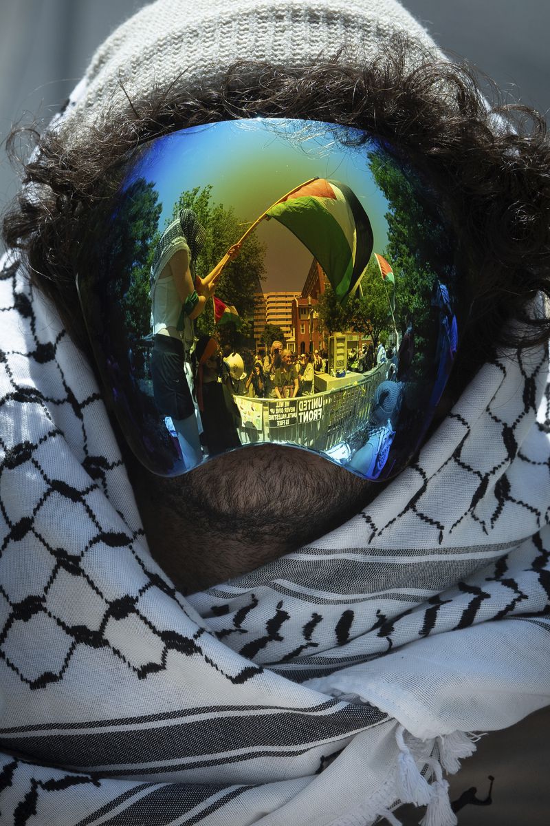 A Palestinian flag is reflected in a demonstrators mask as students protest the Israel-Hamas war at George Washington University in Washington, Sunday, April 28, 2024. Protests and encampments have sprung up on college and university campuses across the country to protest the war. (AP Photo/Cliff Owen)