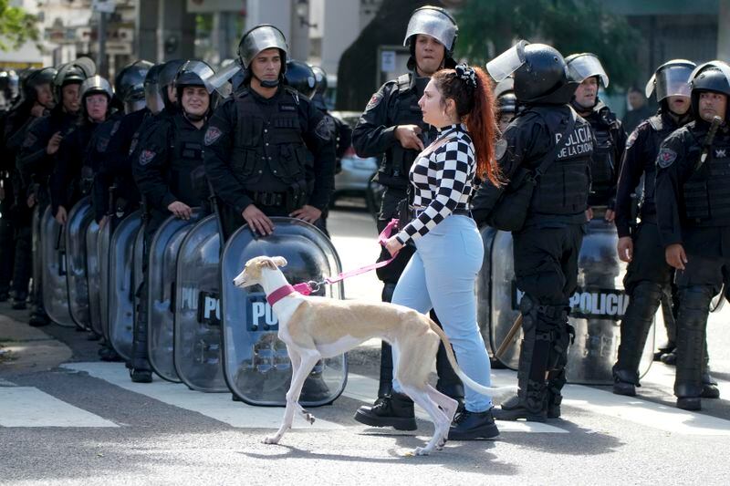 A woman walks her dog past police after they dispersed an anti-government protest against food scarcity at soup kitchens and against economic reforms proposed by President Javier Milei in Buenos Aires, Argentina, Wednesday, April 10, 2024. (AP Photo/Natacha Pisarenko)