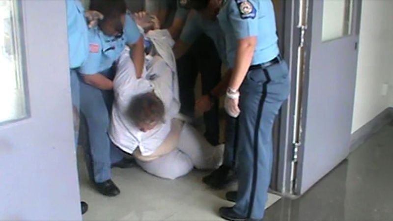 A photo from a prison video shows officers trying to pull inmate Mollianne Fischer to her feet and get her to walk to an isolation cell. Her arms were handcuffed behind her back at the time.