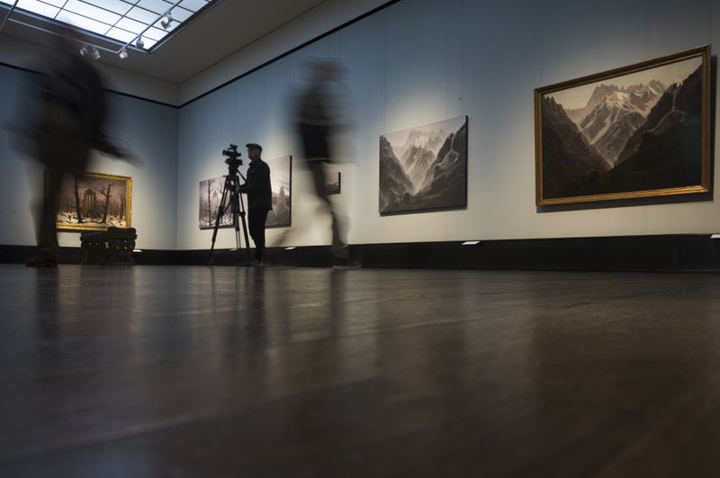 People walk in front of a copies of Caspa David Friedrich's paintings Monastery Cemetery In Snow' , left, and 'High Mountains', right, during a press preview of the exhibition 'Caspar David Friedrich. Infinite Landscapes' at the Alte Nationalgalerie museum in Berlin, Germany, Wednesday, April 17, 2024. A major show of Caspar David Friedrich's iconic landscapes that marks the 250th anniversary of his birth is opening in Berlin, the city where he made his breakthrough and where an exhibition in 1906 kicked off an an enduring revival in interest in the German Romantic master. (AP Photo/Markus Schreiber)