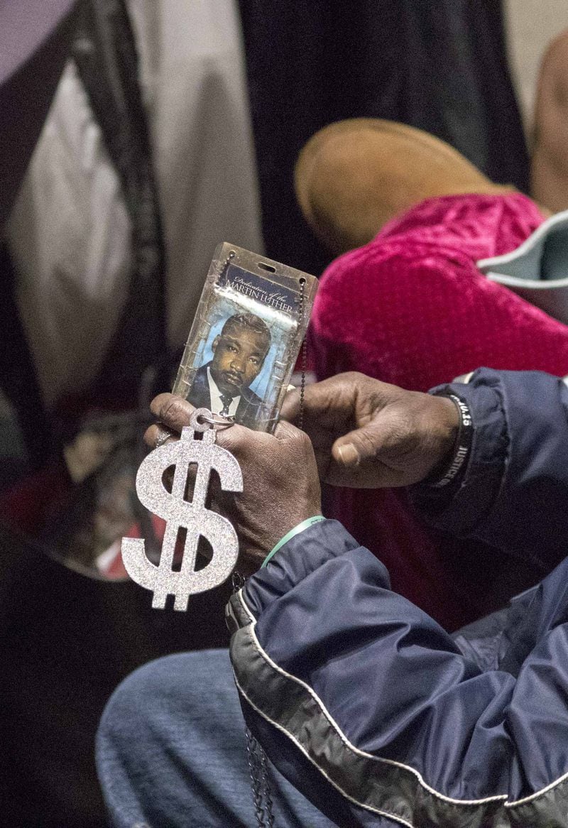 A man holds a photo of Martin Luther King Jr. and a dollar sign pendant as he sits in the audience during the Atlanta City Council meeting on Monday, December 4, 2017. ALYSSA POINTER/ALYSSA.POINTER@AJC.COM