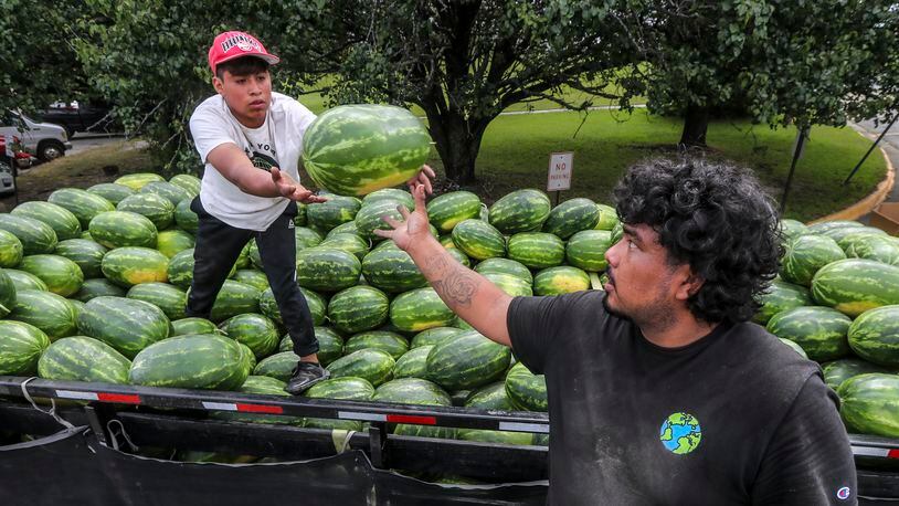 PM Produce workers, Juan Lopez (left) passes off another watermelon to Daniel Valle (right) as they load up another customer at the Atlanta State Farmers Market in Clayton County located at 16 Forest Pkwy in Forest Park.
