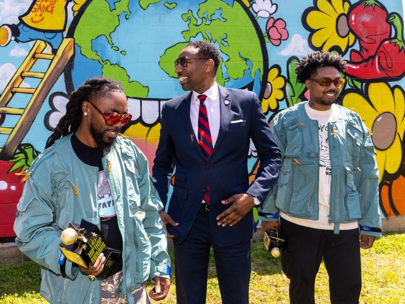 Olu aka Johnny Venus (from left), Mayor Andre Dickens, and WowGr8 aka Doctur Dot stand in front of a mural in a new community garden at Jean Childs Young Middle School in Atlanta on Thursday, March 30, 2023. Olu and WowGr8 of hip-hop group Earthgang helped sponsor the project. (Arvin Temkar / arvin.temkar@ajc.com)