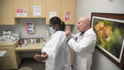 Dr. John Destito, at right, places a protective covering on office manager Kay Hayes at their American Family Care clinic in Buckhead. The two were going through a training for coronavirus procedures. Destito says their intake questionnaire is now screening all patients for factors like travel and coughing that could be indicators for coronavirus. (PHOTO by ALYSSA POINTER/ALYSSA.POINTER@AJC.COM)