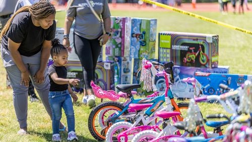 Porche Johnson helps her daughter Sanay Barry, 2,  pick out a new bike during the Fulton County Sheriff's Office bike-a-thon in Atlanta on Saturday, May 11, 2024.   (Steve Schaefer / AJC)