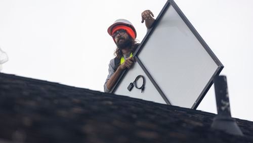 FILE: Joe McClain, an installer for Creative Solar USA, moves solar panels onto the roof of a home in Ball Ground, Georgia on Dec. 17th, 2021. (Nathan Posner for The Atlanta Journal-Constitution)