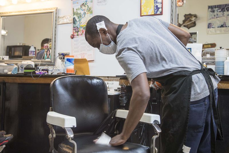 Athens, Georgia  - Wearing a mask, Tony Brown, barber at Brown's Barber Shop, uses a disinfectant wipe to sanitize his chair after servicing a client at the shop in downtown Athens, Friday, April 24, 2020. The family owned small business reopened on Friday, after receiving clearance from Gov. Brian Kemp.  (ALYSSA POINTER / ALYSSA.POINTER@AJC.COM)