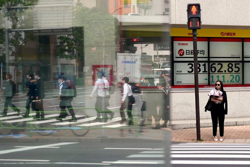 A person stands in front of an electronic stock board showing Japan's Nikkei 225 index at a securities firm as pedestrians are reflected on a glass window Thursday, May 2, 2024, in Tokyo. (AP Photo/Eugene Hoshiko)