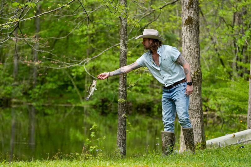 Brian Kelley tosses a fish back into a pond after catching it outside his cabin Wednesday, April 17, 2024, in Nashville, Tenn. (AP Photo/George Walker IV)
