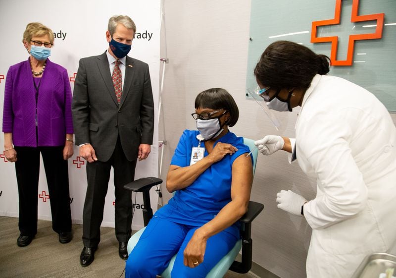 State Public Health Commissioner Dr. Kathleen Toomey and Gov. Brian Kemp look on as Grady ICU nurse Norma Poindexter receives her COVID-19 vaccination Thursday.  Dr. Toomey was vaccinated next. (PHOTO by Steve Schaefer for the Atlanta Journal-Constitution) 
