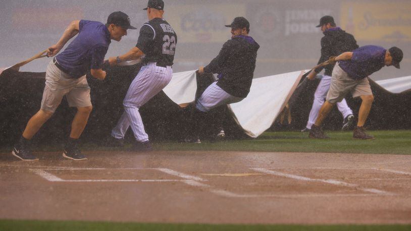 Manager Walt Weiss, catcher Michael McKenry #8 and starting pitcher Chad Bettis #35 of the Colorado Rockies help the grounds crew pull the tarp over the field during a could burst that halted play against the Atlanta Braves in the first inning at Coors Field on July 9, 2015 in Denver, Colorado. (Photo by Justin Edmonds/Getty Images)