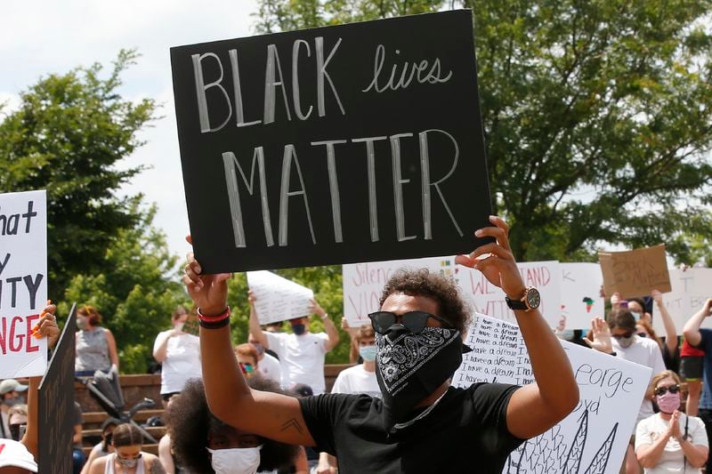 FILE - In this June 1, 2020, file photo, Atlanta Hawks guard Trae Young holds a "Black Lives Matter" sign during a peaceful rally in his hometown of Norman, Okla., calling attention to the killing of George Floyd. While NBA players are using the season restart to demand change; coaches in the league are not making them walk down that path alone. (AP Photo/Sue Ogrocki, File)