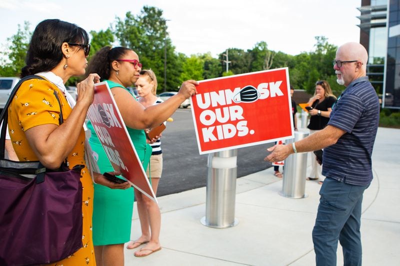 Billy Cahill (far right) hands a woman his "unmask our kids" sign to pose for a photo outside of the Cobb County School District office on May 20, 2021, in Marietta, Georgia . Many community members waited in line to speak at the school board meeting to voice their support for unmasking.  CHRISTINA MATACOTTA FOR THE ATLANTA JOURNAL-CONSTITUTION