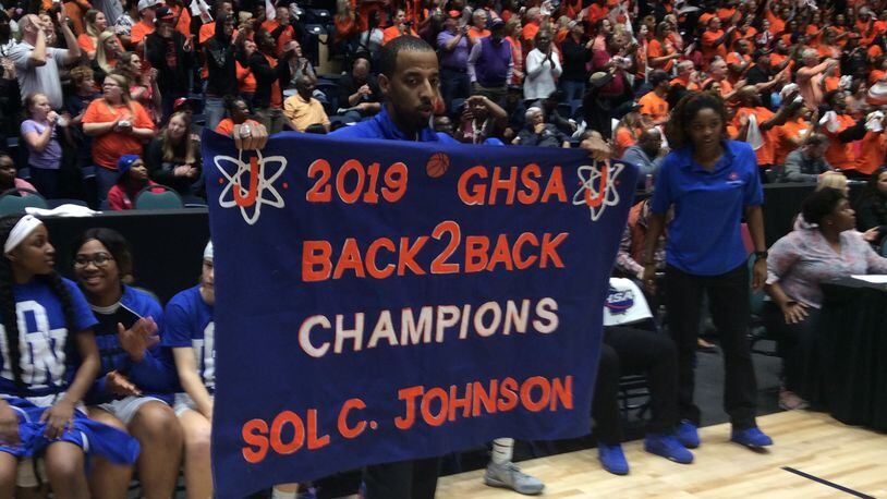 Johnson-Savannah girls coach Brandon Lindsey displays the banner proclaiming his team's back-to-back state championships after a 54-50 victory over Hart County in the Class AAA final Thursday at the Macon Coliseum.