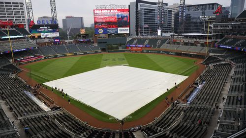 Ground crew workers are finishing putting the tarp to cover the diamond at Truist Park as raindrops started to fall moments before the second game of the series between the Atlanta Braves and the New York Mets on Tuesday, April 9, 2024. (Miguel Martinez / miguel.martinezjimenez@ajc.com)