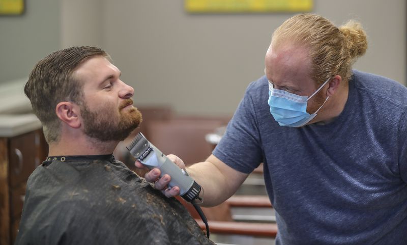 Barber and shop owner Chris Edwards wears a mask and cuts the hair of customer David Boswell at Peachtree Battle Barber Shop at 2333 Peachtree Road in Atlanta on Friday, April 24, 2020. The first phase of Gov. Brian Kemp's plan to reopen Georgia during the coronavirus pandemic included barber shops, hair salons and gyms, though not all chose to open their doors. JOHN SPINK/JSPINK@AJC.COM