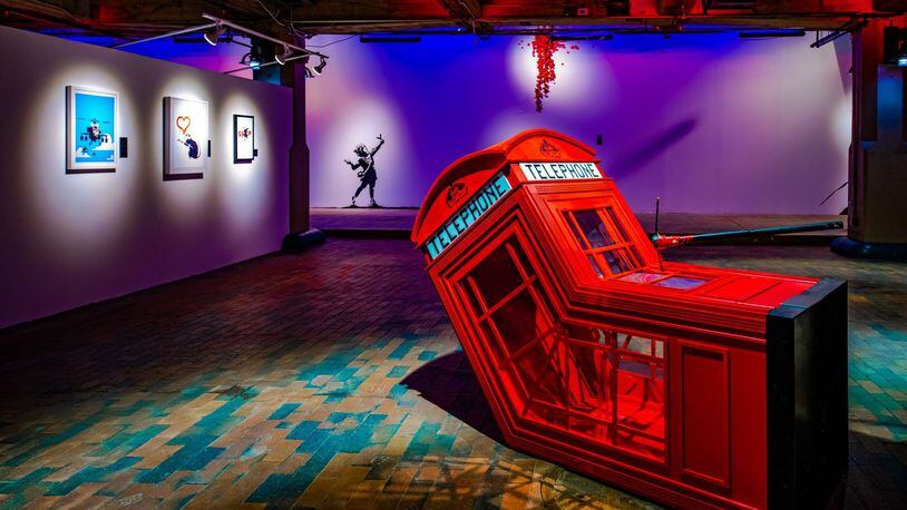 The 2006 Banksy sculpture "Death of a Phone Booth" is framed by three prints and a recreation of the 2020 mural "Valentine's Day" painted by local artists at The Art of Banksy: "Without Limits" exhibition in Underground Atlanta. Lola Scott Art/SEE Global Entertainment