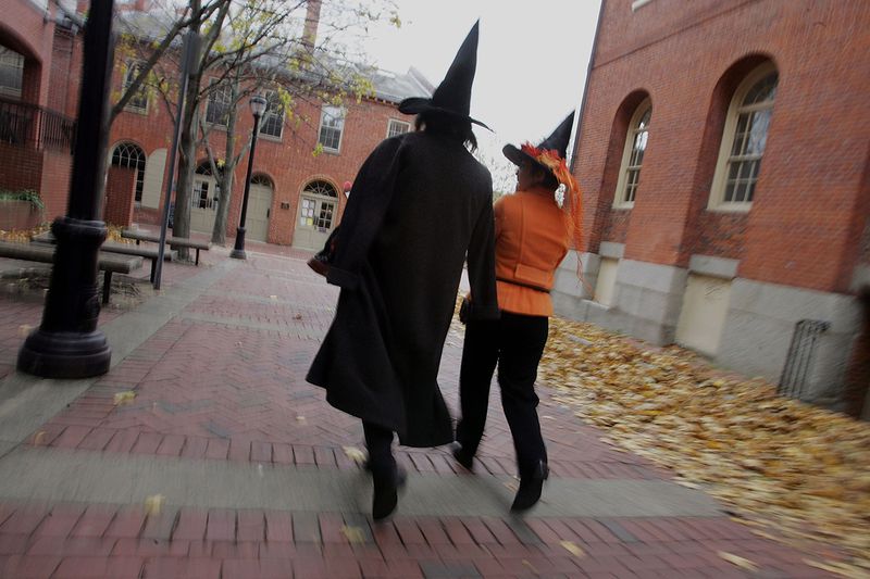 Costumed people dressed as witches walk though the street next to the old Town Hall as they visit the town where, back in 1692, witch trials took place, October 27, 2005  in Salem, Massachusetts. Thousands of tourists come to attend the large Halloween festival.  (Photo by Joe Raedle/Getty Images)